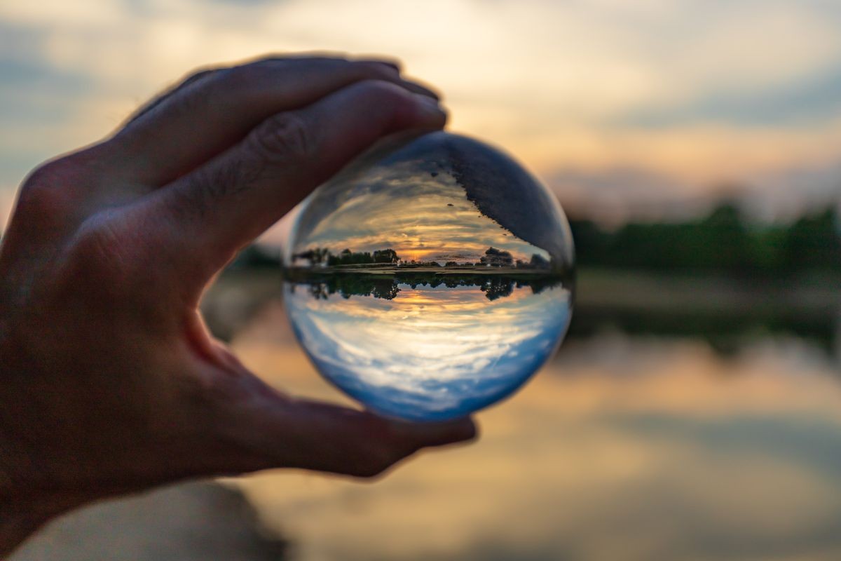 A clear glass ball being held with a sunset able to be seen through it with a silky smooth, bokeh background.